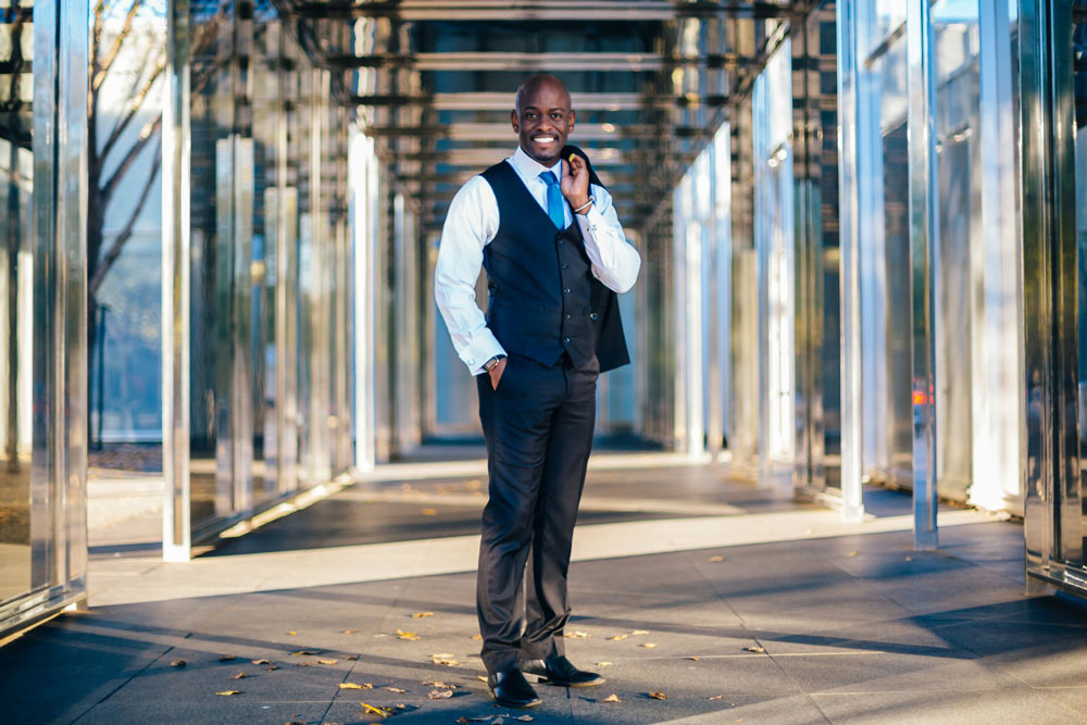 Brian in a professional suit, posing in front of the NC Museum of Art’s architecture