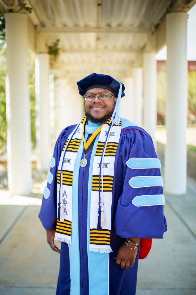 headshot in cap and gown on nc state campus in doctoral regalia