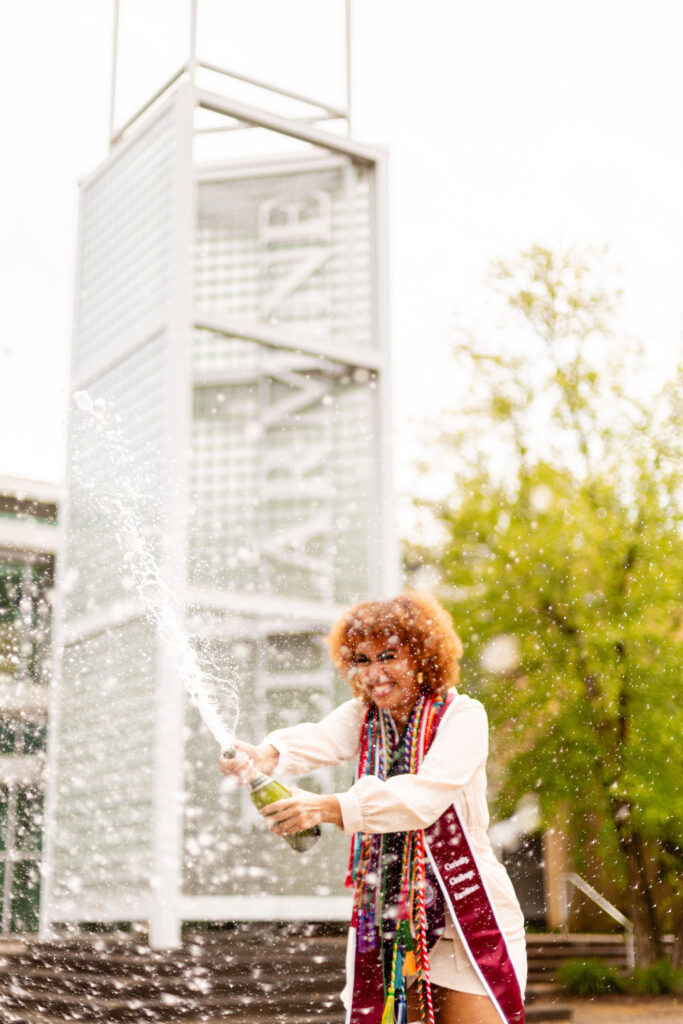 bellarmine university student popping a bottle of champagne to celebrate graduation during photoshoot