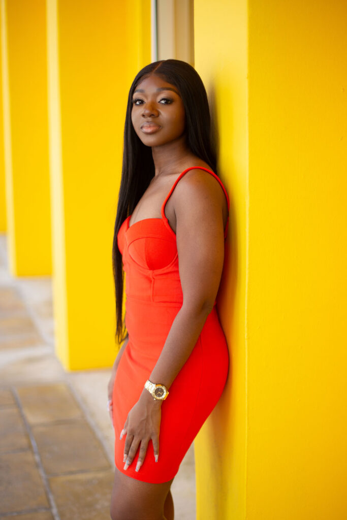 Woman taking birthday pictures in orange bodycon dress with yellow walls outside Fendi store in Miami Design District.