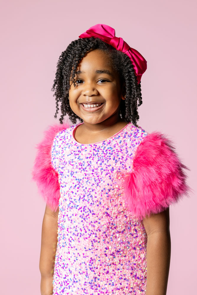 Kennedy posing in sparkly dress with fur sleeves during her 5th birthday photoshoot on a pink backdrop.