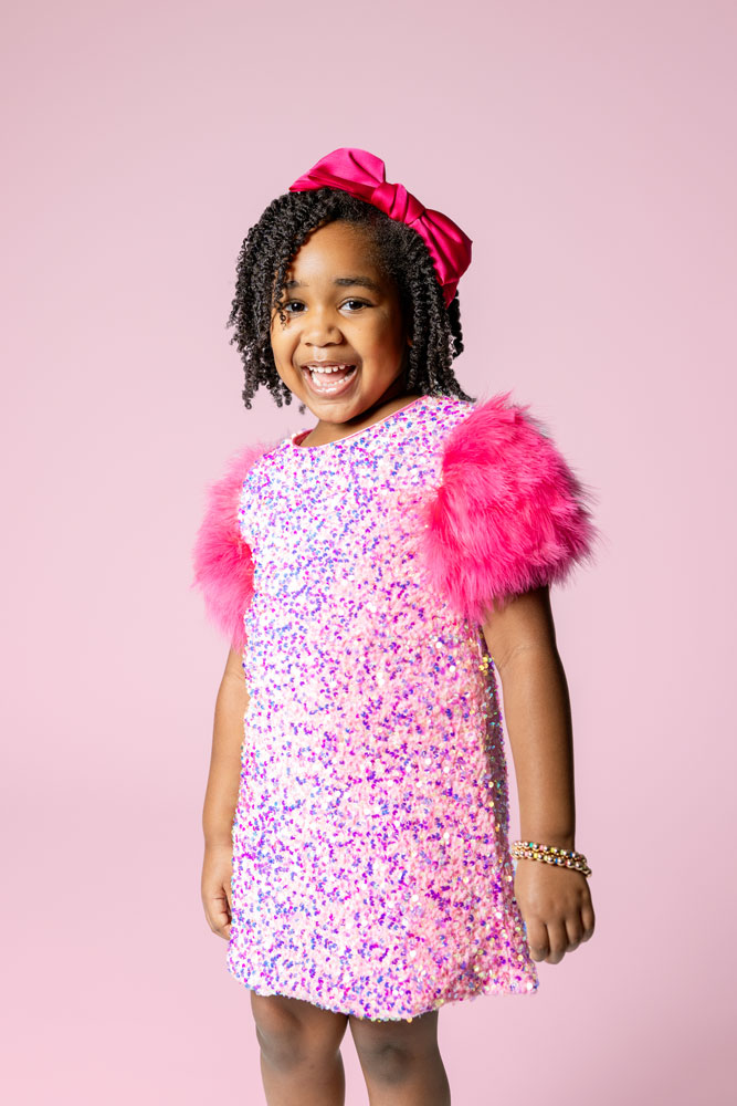 5th birthday photoshoot with pink background and sparkly dress with fur sleeves.