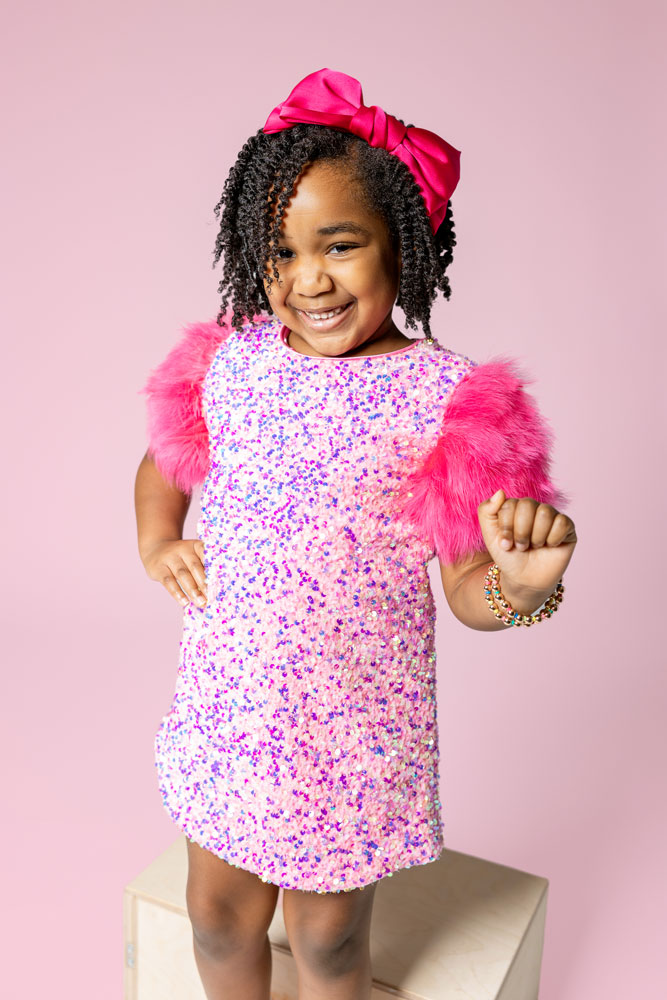 Fun, sassy, and vibrant birthday photo with sparkly dress and fur sleeves on a pink background.