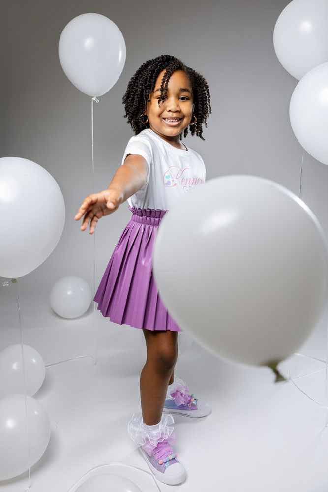 Kennedy playing with a white balloon in a purple leather pleated skirt and personalized t-shirt for her 5th birthday photoshoot.