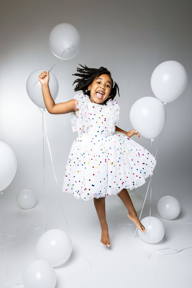 Fun 5th birthday photo of Kennedy jumping with a white balloon in a confetti print dress.