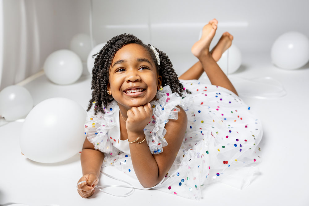 Kennedy posing with white balloons in a white dress with confetti print for her 5th birthday photoshoot.