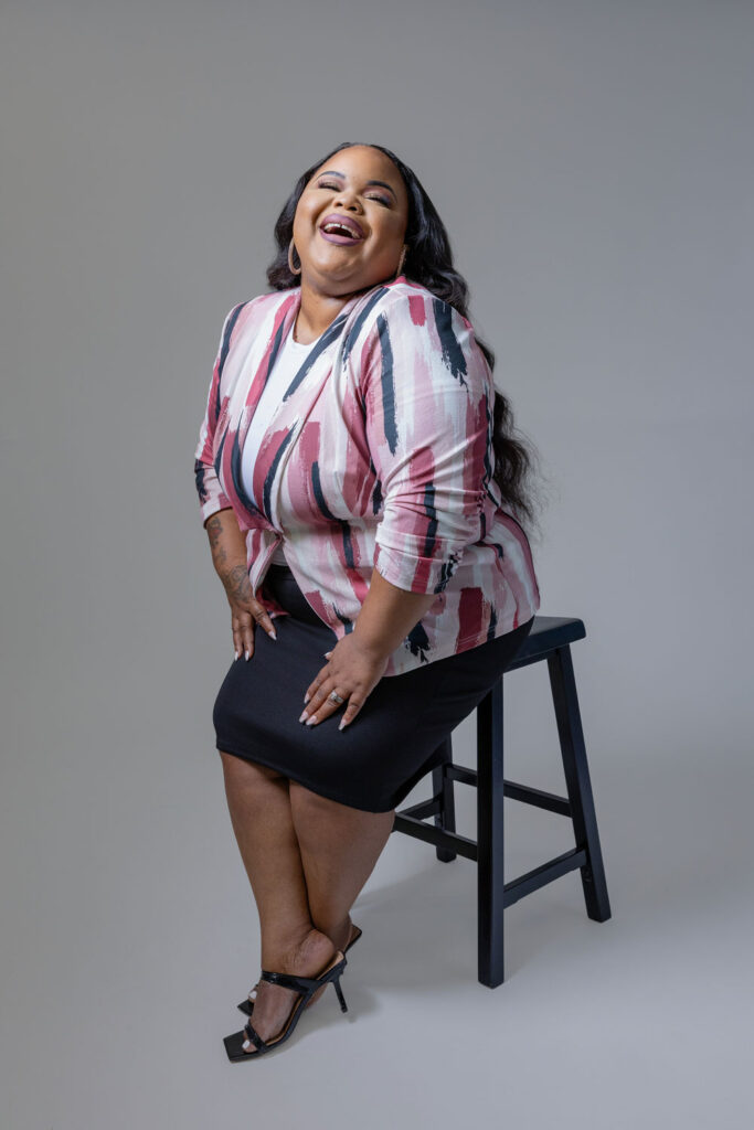 Full-body photo of Madilla from Medallion Styles, laughing while sitting on a stool during her brand photoshoot in Raleigh