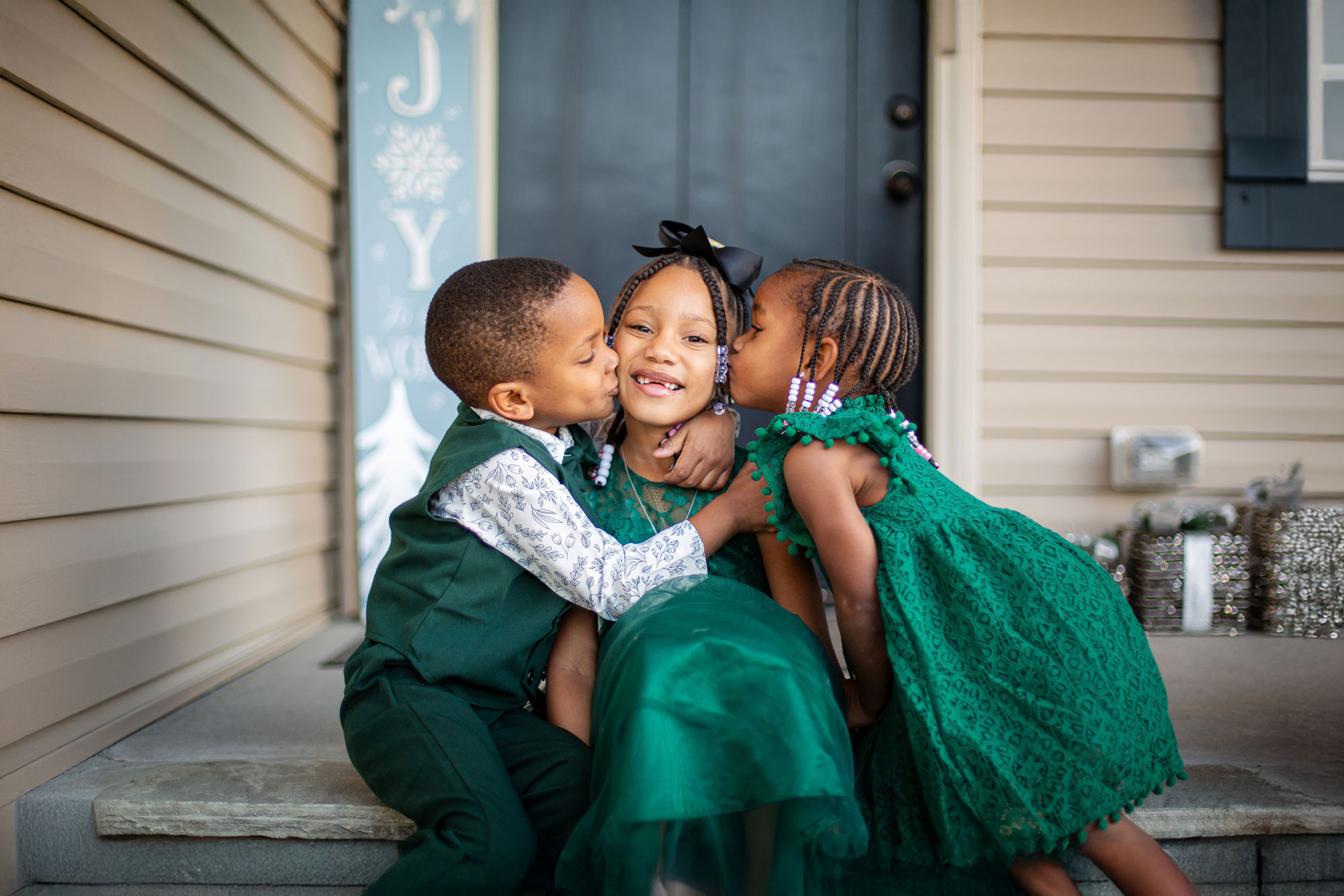 Capturing sibling love during a Christmas mini session, as the younger siblings kiss their big sister on both cheeks