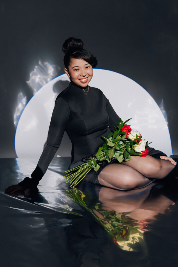 Black girl sitting on floor posing with roses on her lap during spotlight birthday photoshoot in raleigh nc