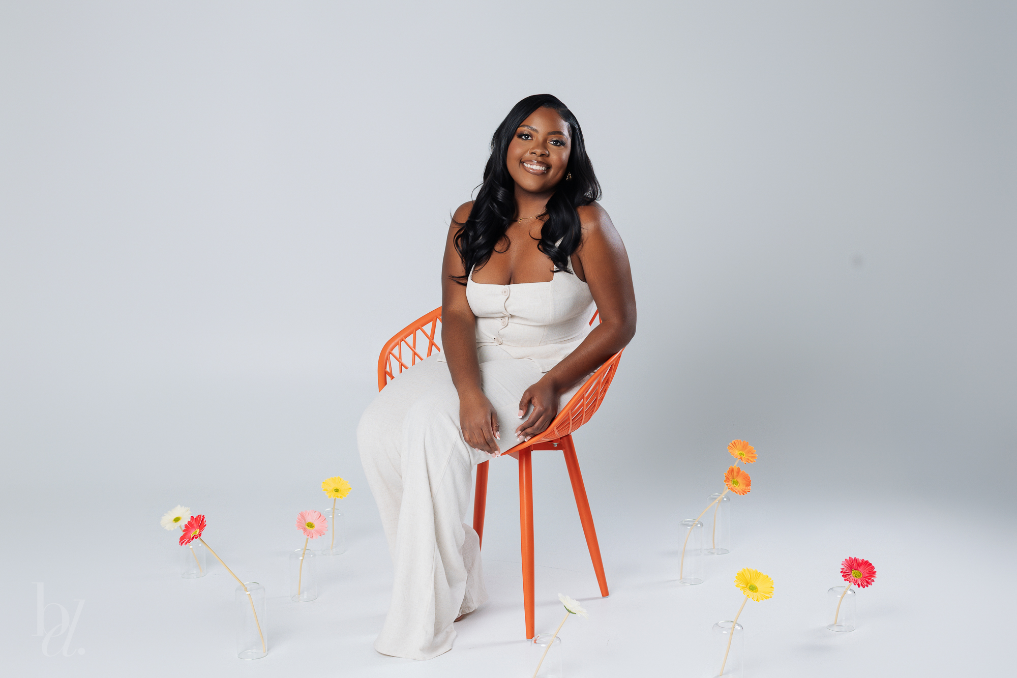 Black author sitting in orange chair surrounded by flowers in vases – creative Raleigh NC branding photos