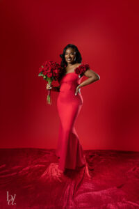 Woman posing confidently in a red gown holding roses on a red backdrop at a birthday photoshoot in Raleigh.
