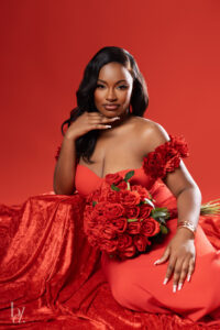 Close-up portrait of a woman in a red dress holding roses against a red backdrop during a Raleigh birthday photoshoot.