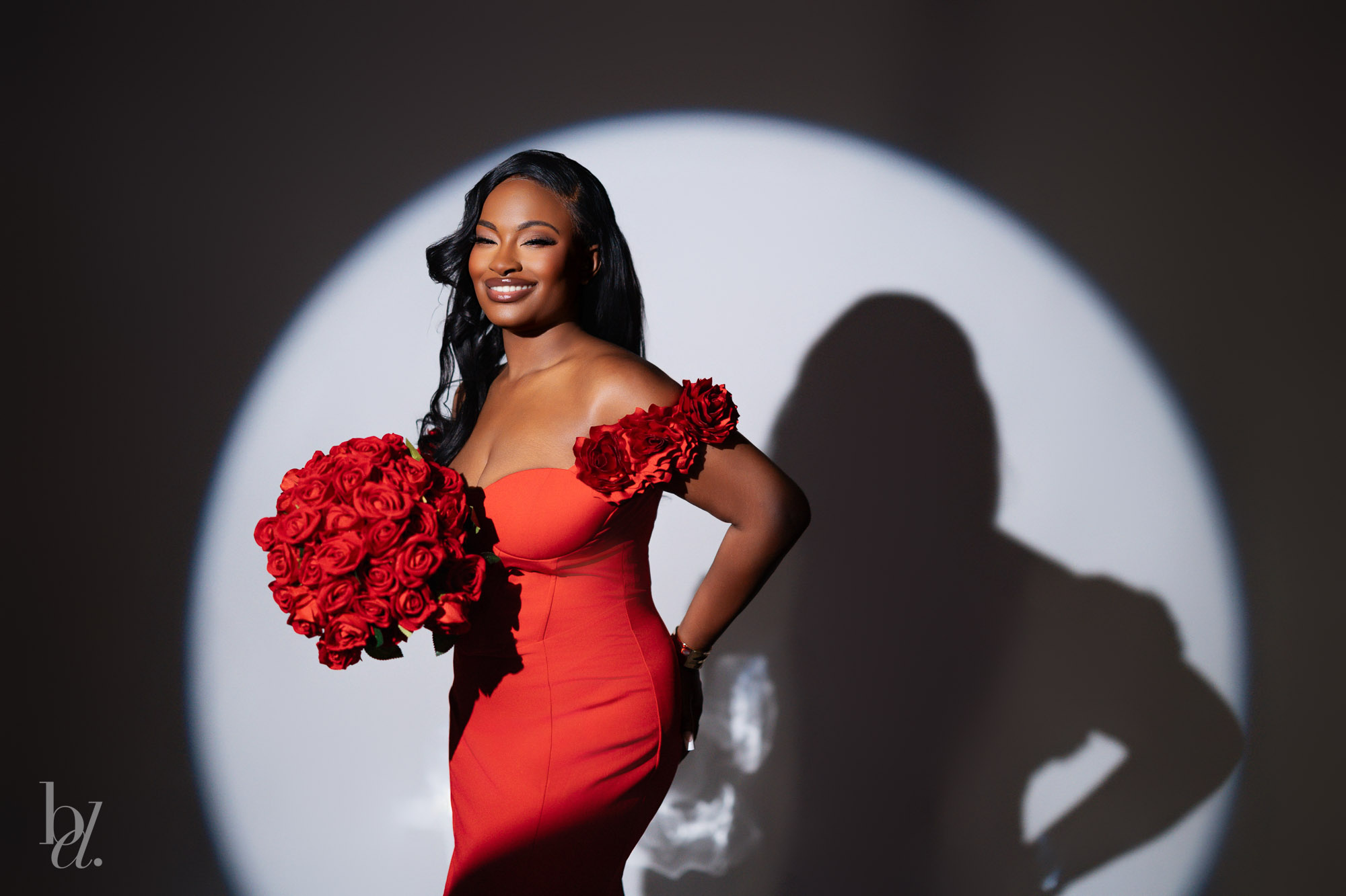 Woman smiling in a red gown with roses while posing inside a dramatic spotlight at a birthday photoshoot in Raleigh.