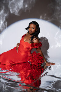 Woman reclining in a red gown with roses on a reflective floor under a circular spotlight during a Raleigh birthday photoshoot.