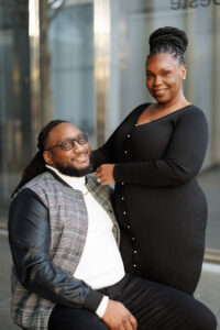 A woman standing confidently beside her seated partner, both smiling gently during an elegant Raleigh engagement photo