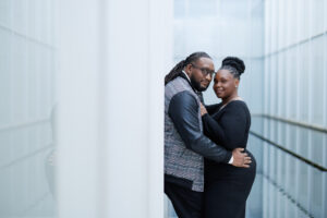 A couple posed together in a long glass corridor, styled in a modern editorial engagement photo in Raleigh North Carolina