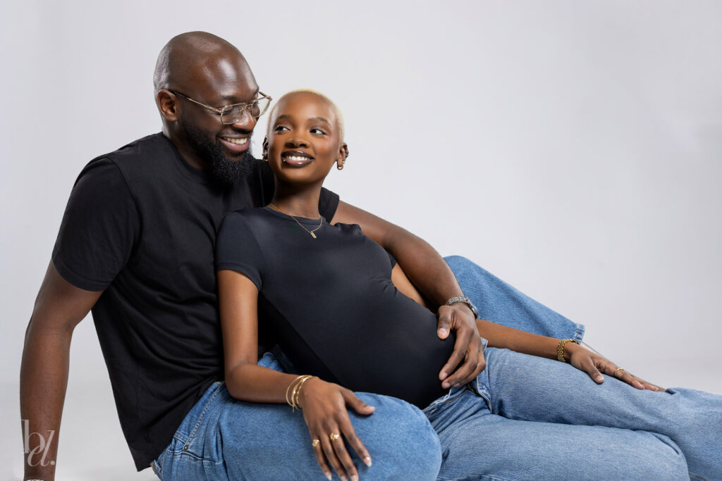Joyful maternity studio photo of expecting couple seated together on white backdrop in Raleigh