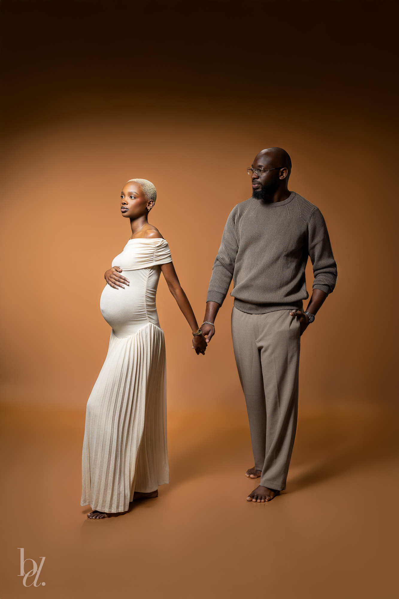 Elegant studio maternity portrait of expecting couple holding hands on warm brown backdrop in Raleigh
