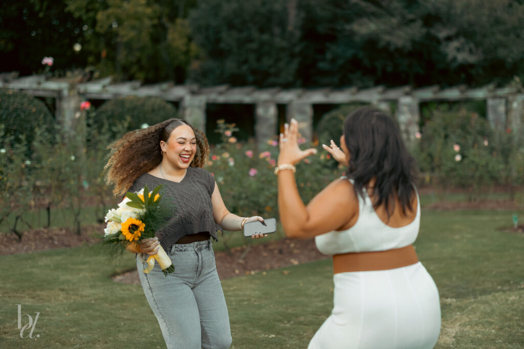 A close friend approaching with flowers to celebrate a surprise proposal at the Raleigh Rose Garden.