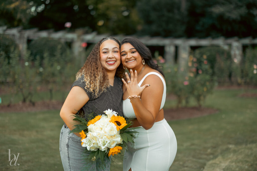Two friends smiling together during post-proposal photos at a Raleigh engagement session, engagement ring visible.