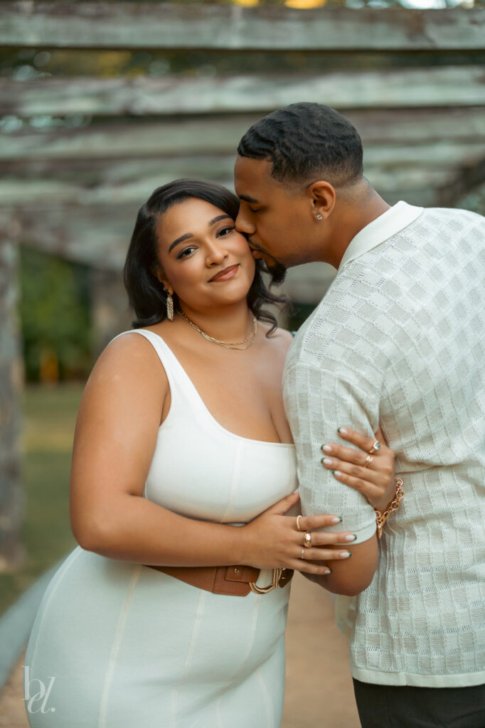 One partner kissing the other’s cheek during a relaxed engagement photoshoot at the Rose Garden in Raleigh.