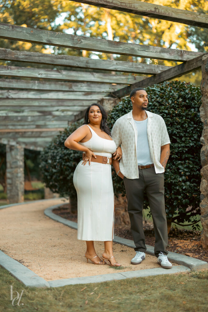Couple posing confidently beneath a garden pergola during an engagement session at the Raleigh Rose Garden.