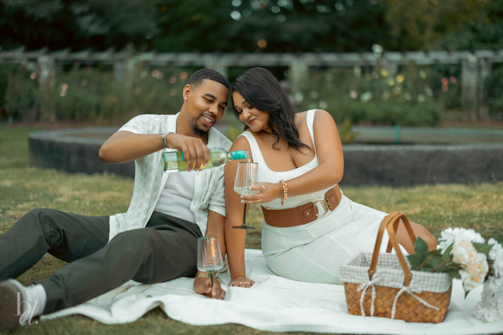 Picnic setup with wine being poured during an engagement photo session at the Rose Garden in Raleigh.