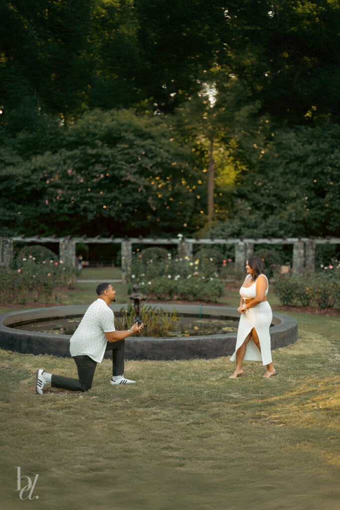 Wide view of a surprise proposal near the fountain at the Raleigh Rose Garden during an engagement shoot.