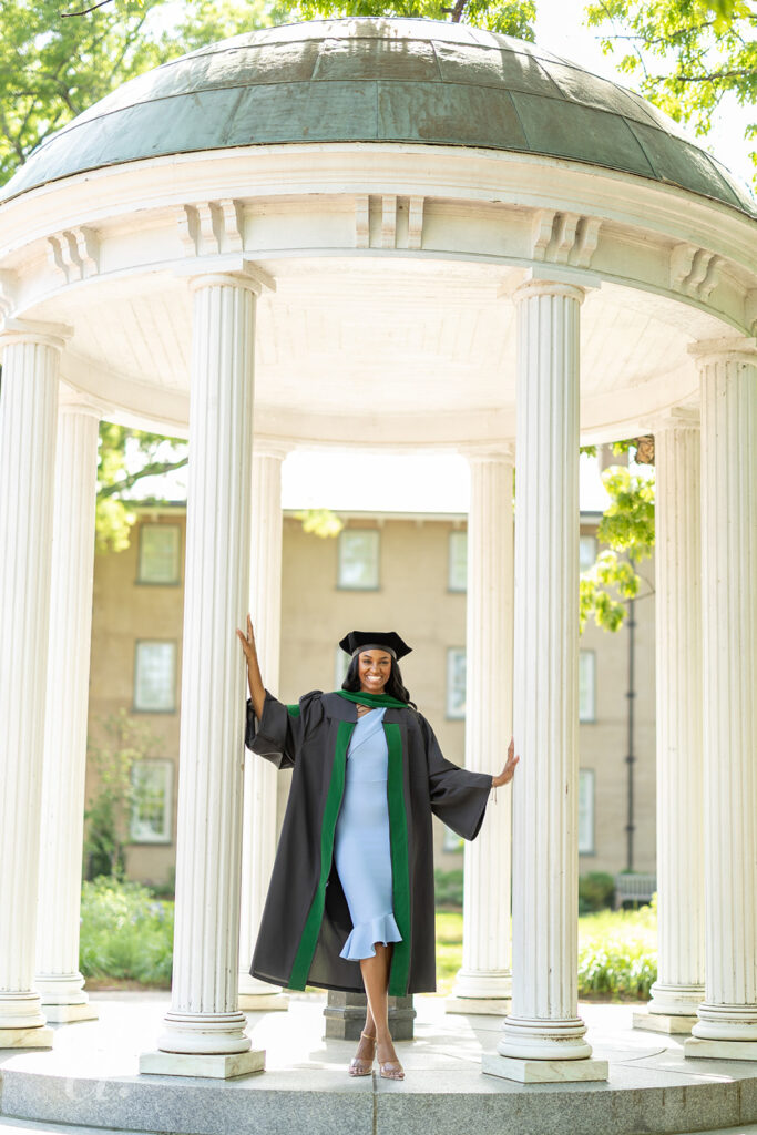 doctoral graduate posing at UNC Old Well columns in cap and gown