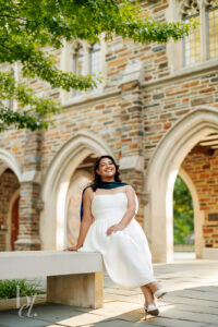 Duke DPT graduate sitting on bench outside Duke Chapel in white dress and regalia