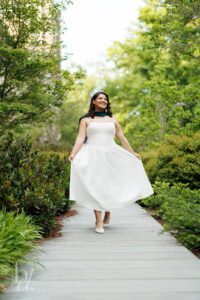 Duke doctoral graduate walking through greenery in white dress holding skirt during grad session