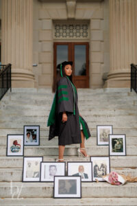 Doctoral graduate standing on UNC Wilson Library steps surrounded by family ancestor portraits