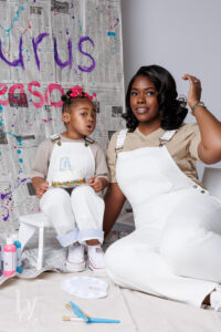 Mommy and me pose with birthday cake in front of a painted newspaper backdrop