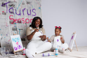 Mother and daughter laughing while painting canvases during a creative Mommy and Me birthday photo shoot