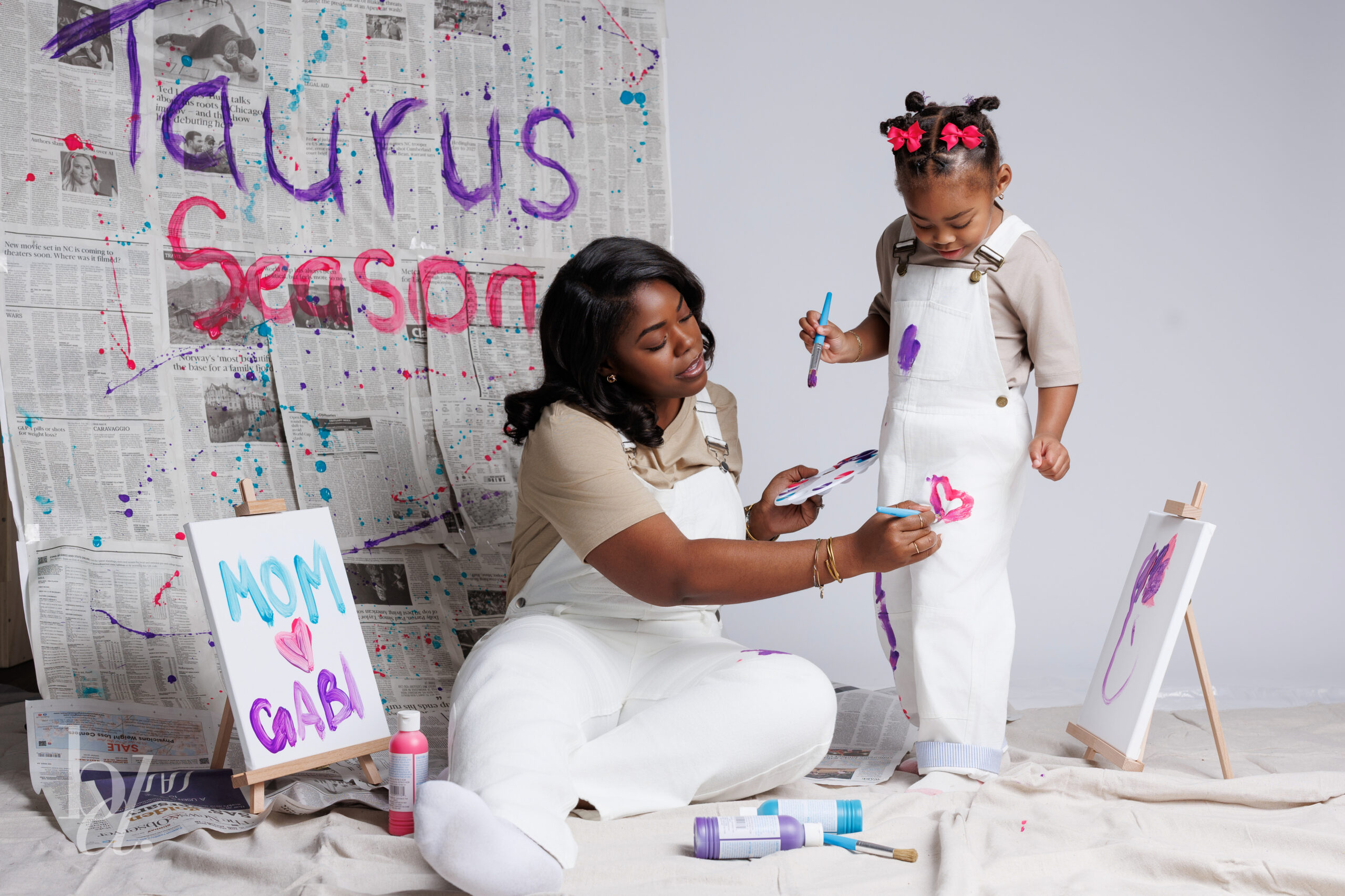 Mother painting a heart on her daughter’s white overalls during a mommy and me creative birthday shoot