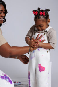 Child pressing a painted handprint onto white overalls during a birthday paint session