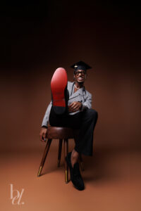 Graduate laughing with the sole of a dress shoe toward the camera in studio.
