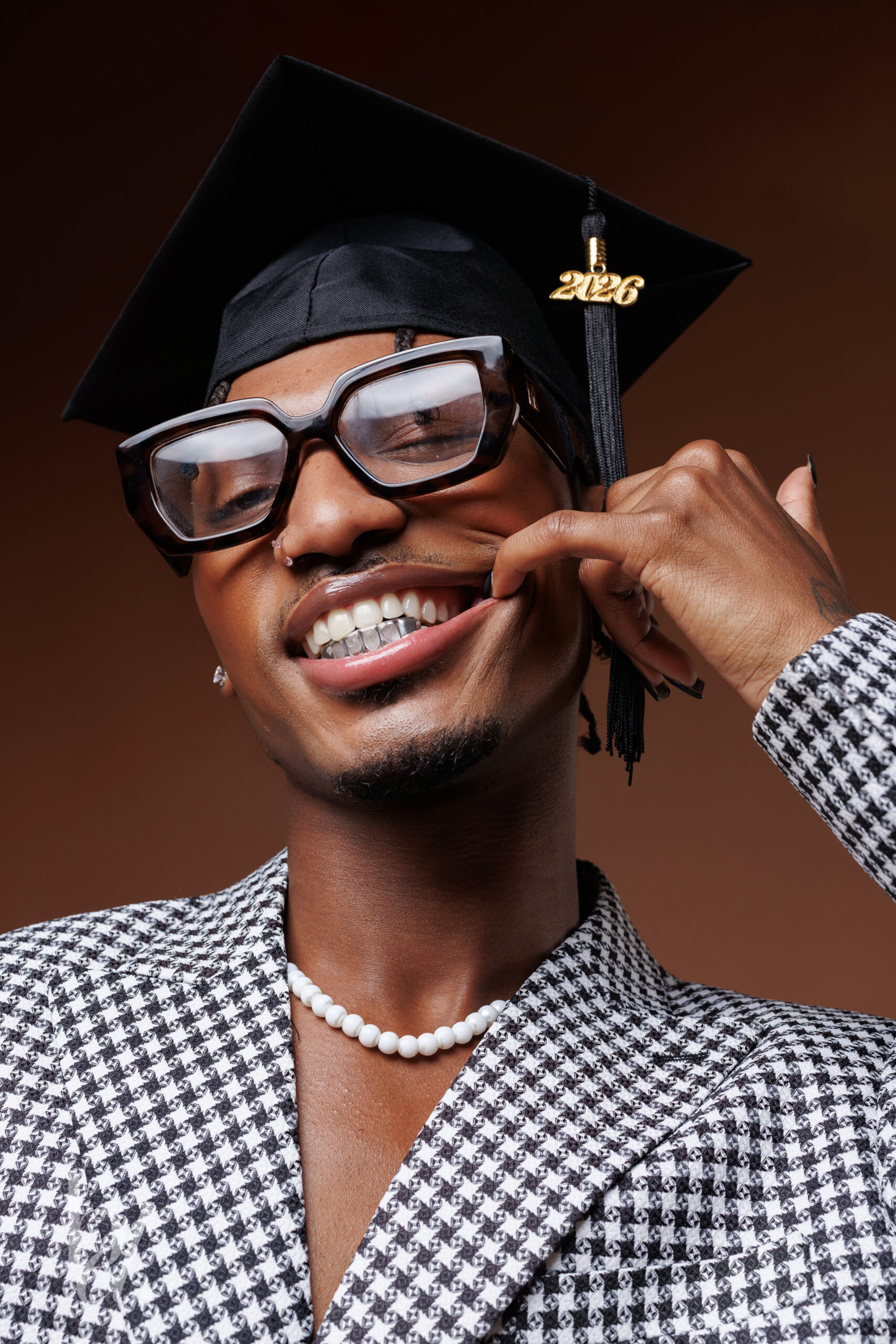 Close-up graduation portrait featuring glasses, graduation cap, and a 2026 tassel and silver grill.