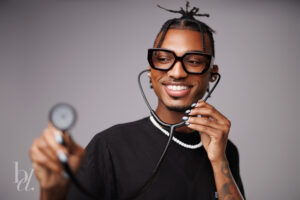 Graduate smiling while listening through a stethoscope during a studio graduation photoshoot.